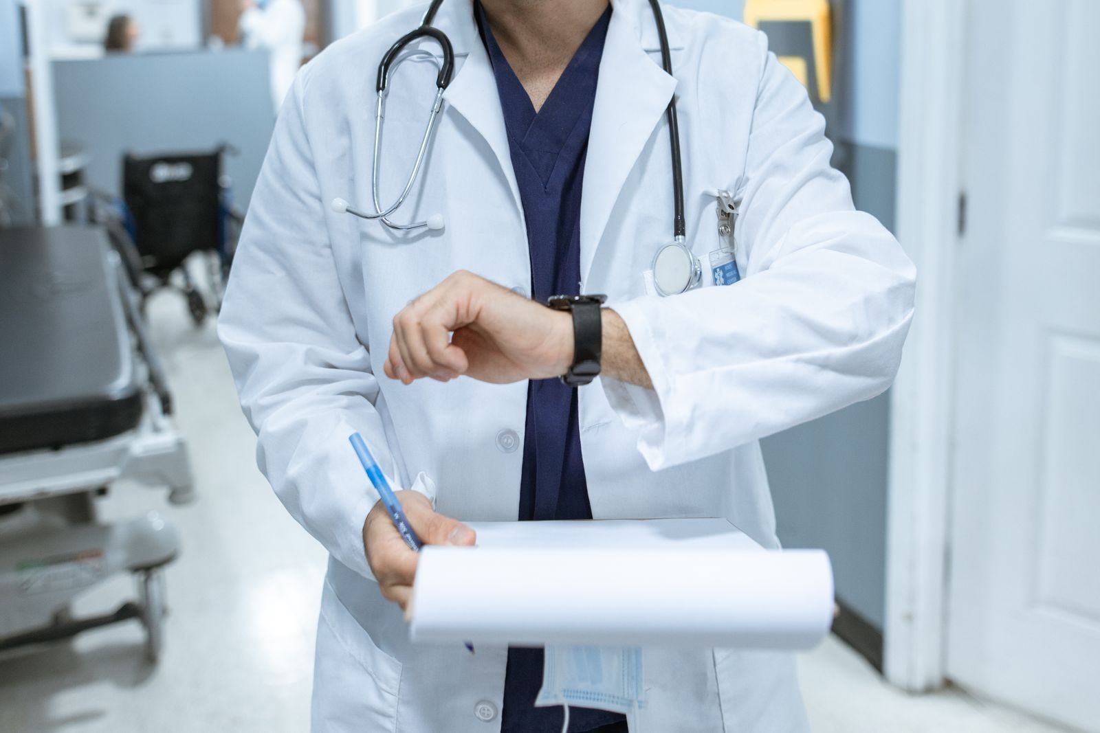 Lekár v bielom plášti sa pozerá na hodinky na chodbe ambulancie